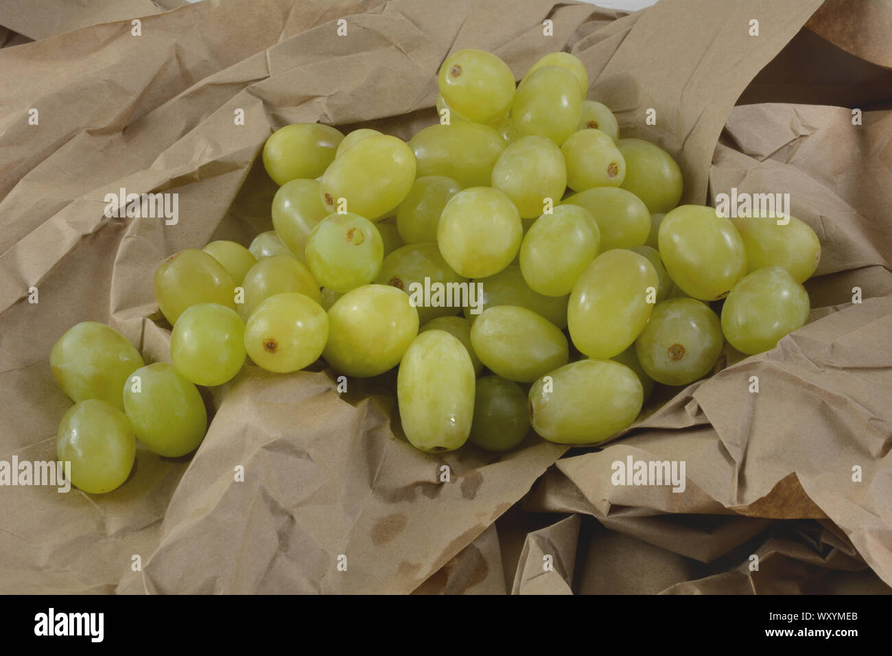 Tas de raisins verts fraîchement rincée au large de tige sur du papier froissé et plié brown Banque D'Images