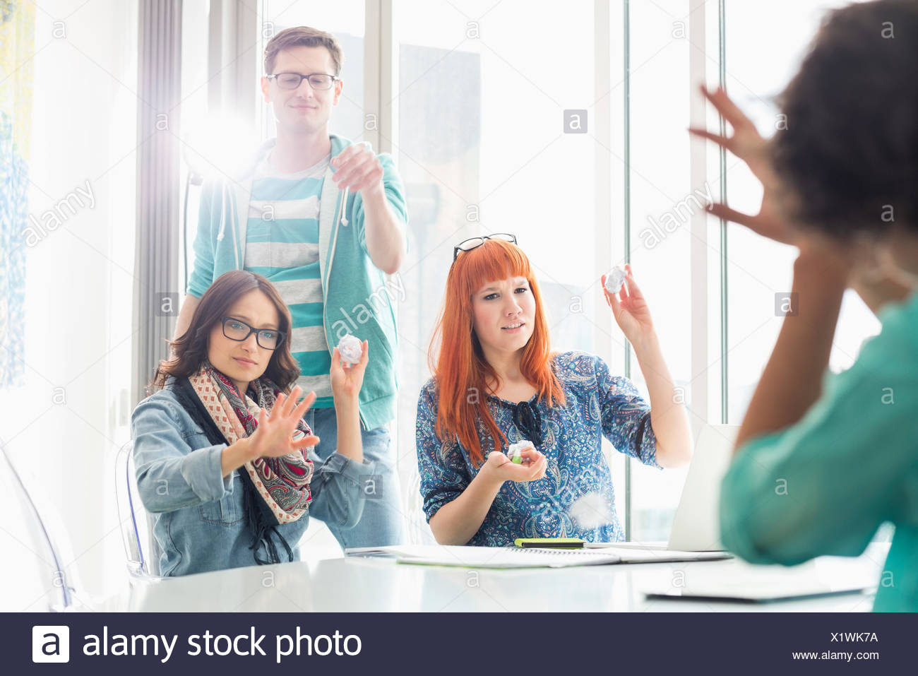 Angry woman throwing paper balls sur collègue in creative office Banque D'Images