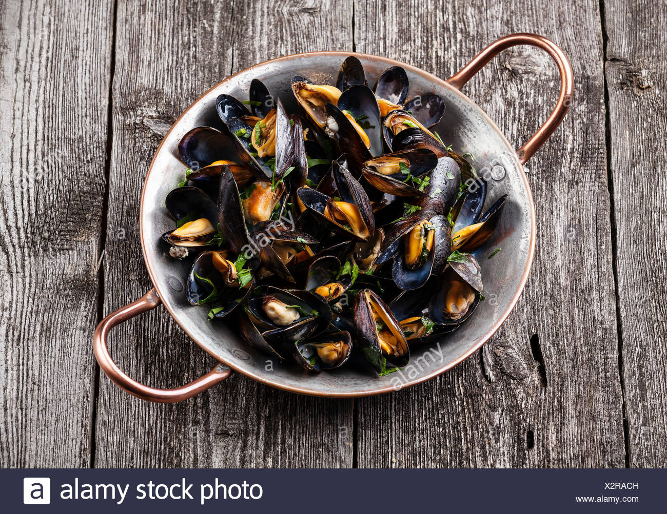 Les moules cuites dans un plat de cuisson en cuivre foncé sur fond de bois Banque D'Images