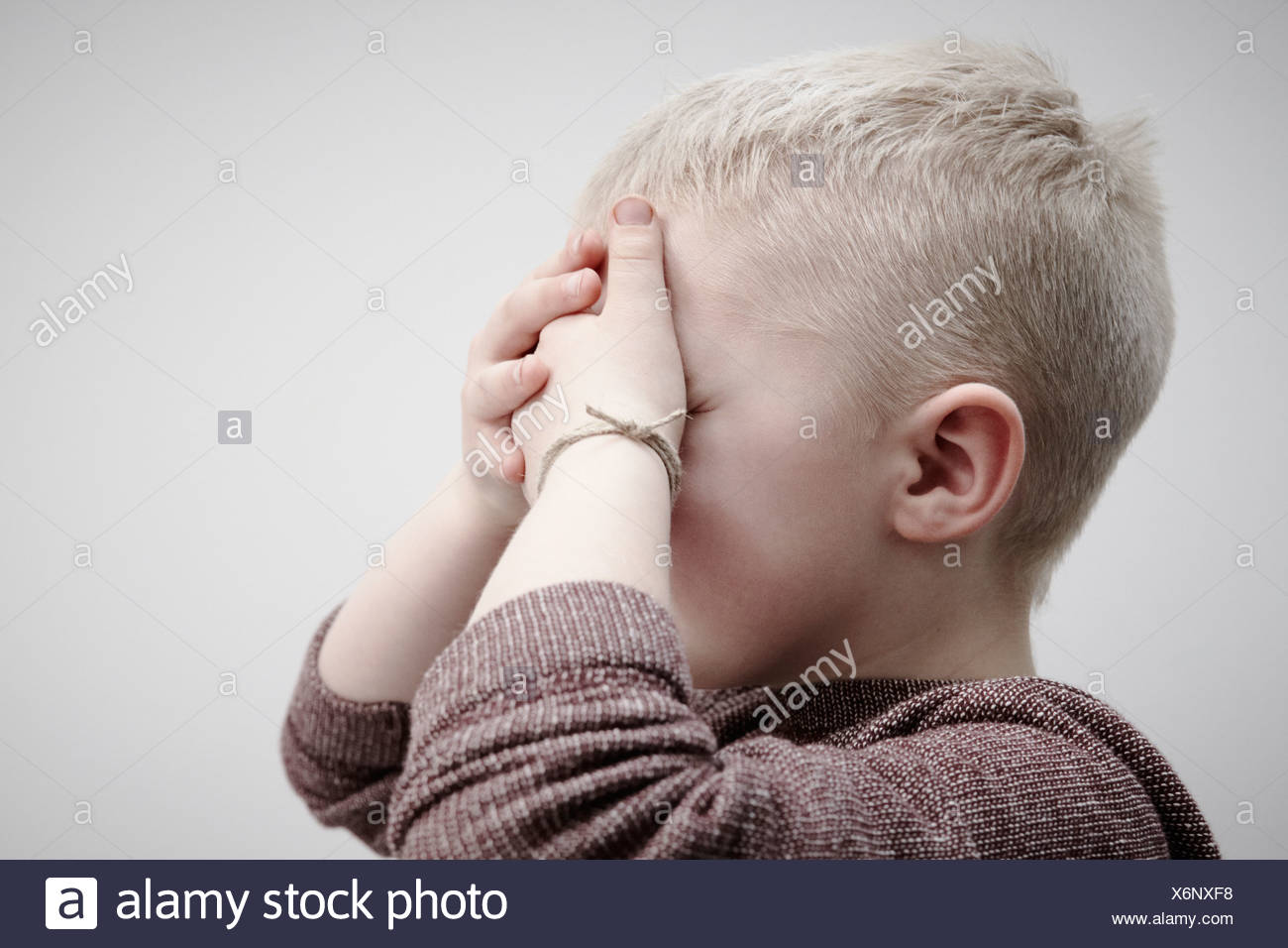 Portrait of boy wearing brown cavalier, couvrant le visage avec les mains Banque D'Images