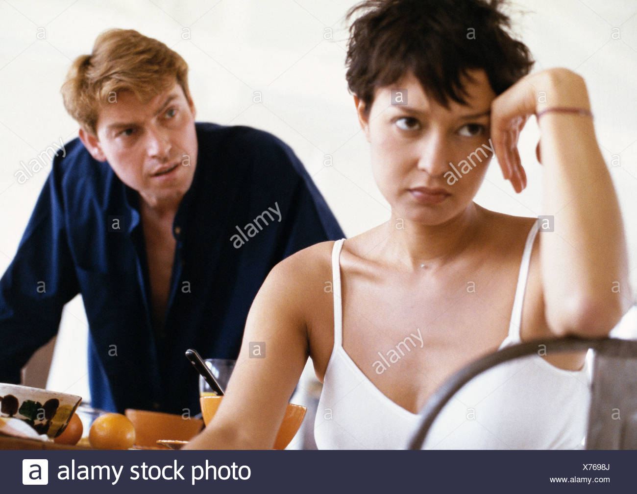 Femme assise, le coude sur le dos de chaise, main contre la tête, l'homme se penchant vers son en arrière-plan, vue avant Banque D'Images