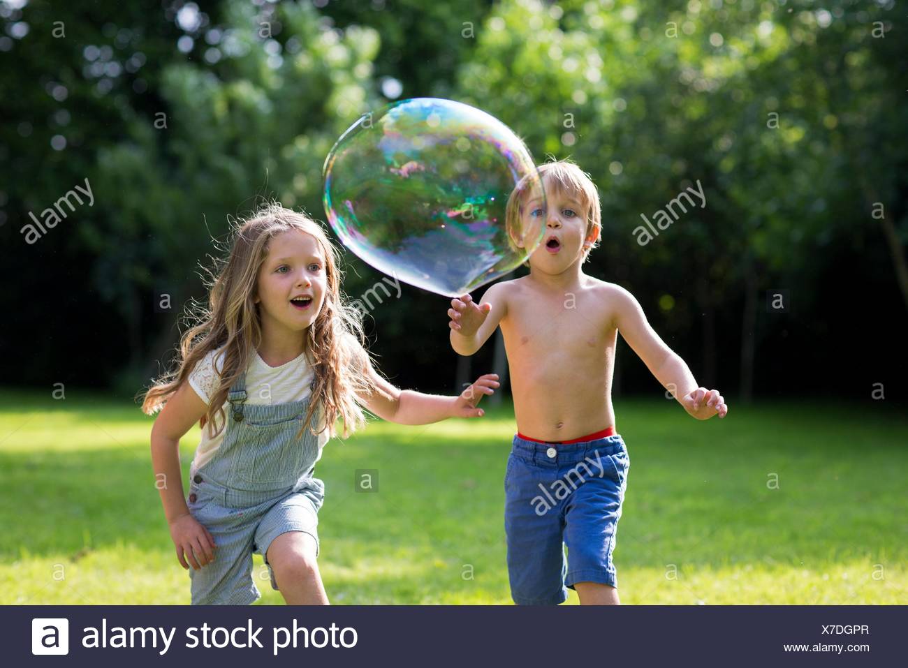 Parution de la propriété. Parution du modèle. Frère et sœur chassant bulles dans le jardin. Banque D'Images