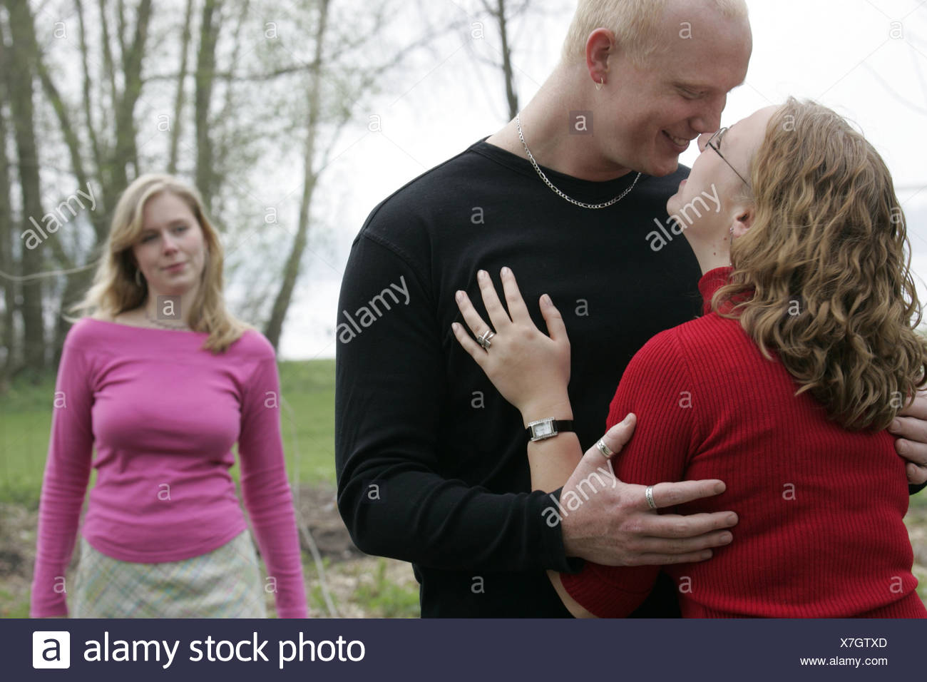 Young woman looking at young couple hugging et flirter à l'extérieur, il pourrait être jaloux ou envieux. Banque D'Images