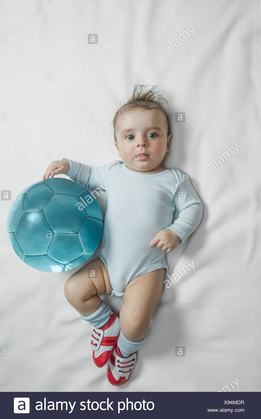 Un petit garçon portant des chaussures de foot bébé couché à côté d'un  ballon de foot Photo Stock - Alamy