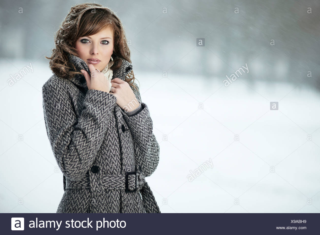Portrait d'une jeune femme dans la neige, sa main tenant son collier manteau Banque D'Images