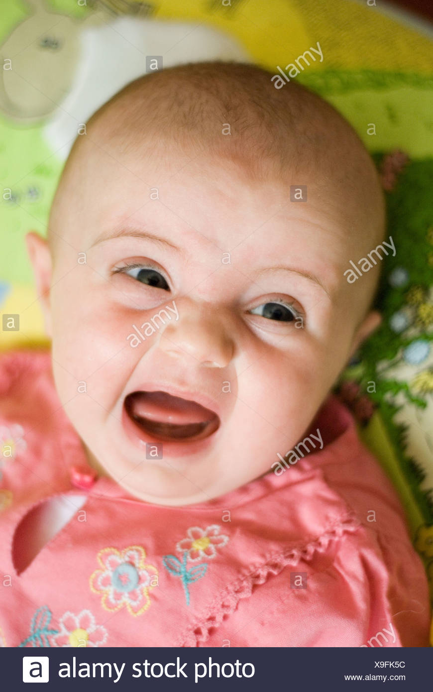 Une Femelle Bebe Assis Contre Un Coussin A Motifs Porte Une Robe De Coton Rose Avec Sa Bouche Ouverte Et De Pleurer Photo Stock Alamy