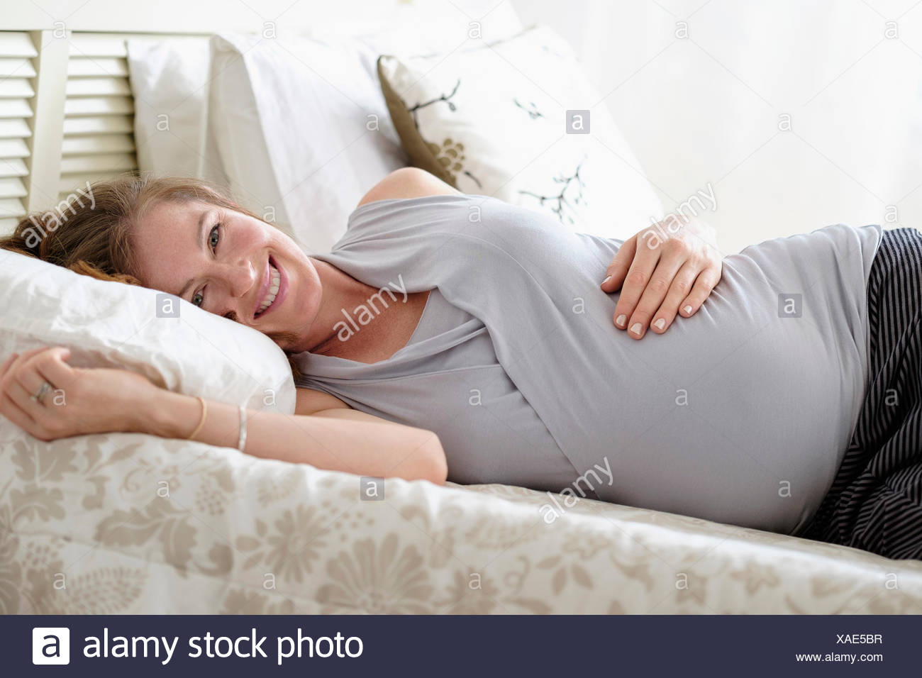 Smiling pregnant woman lying on bed Banque D'Images