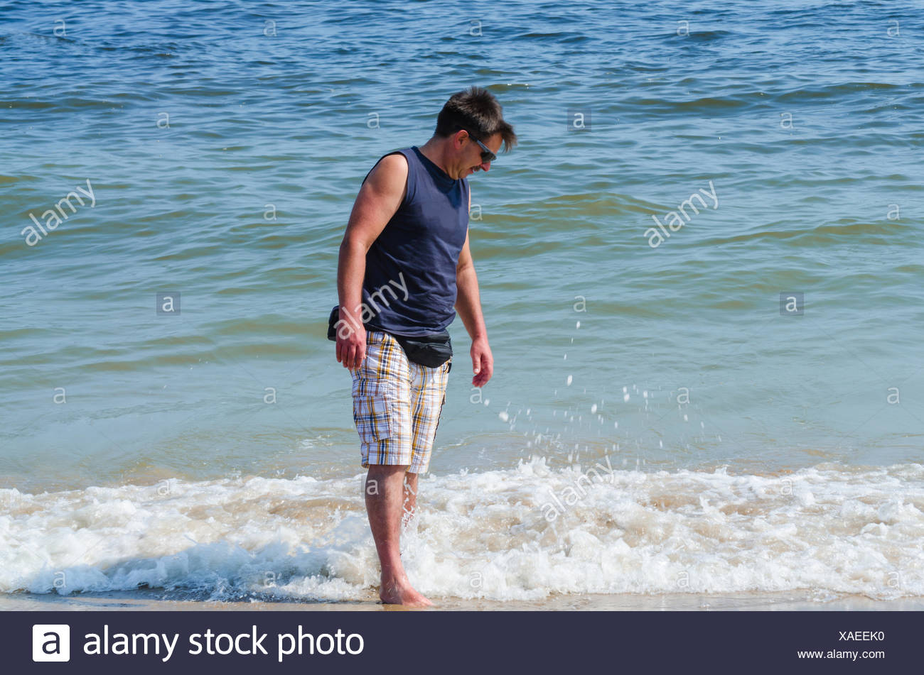 Mann en short, T-shirt brille und mit den Füßen im Wasser. Banque D'Images