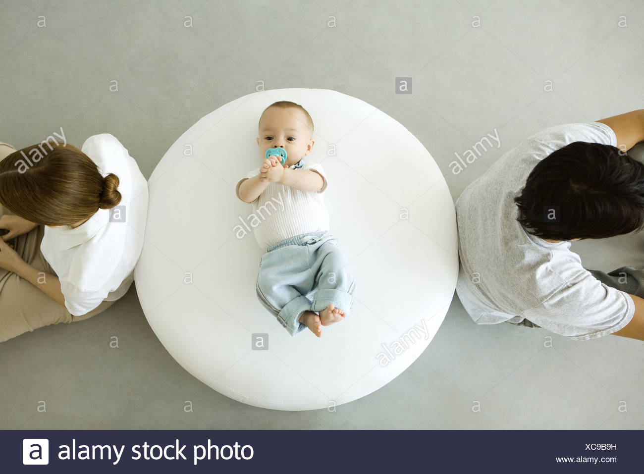 Bébé couché sur un pouf, mère et père assis avec dos tourné, overhead view Banque D'Images