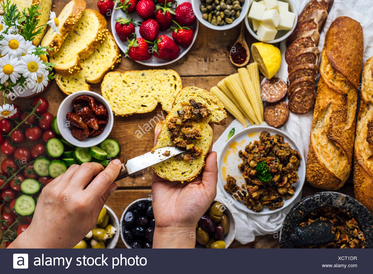 Une Femme La Diffusion De Tapenade D Olives Sur Une Tranche De Pain De Mais Baguette Francaise Saucisses Fromage Cors Bebe Strawberr Es Fleurs Tomates Et Concombre Photo Stock Alamy