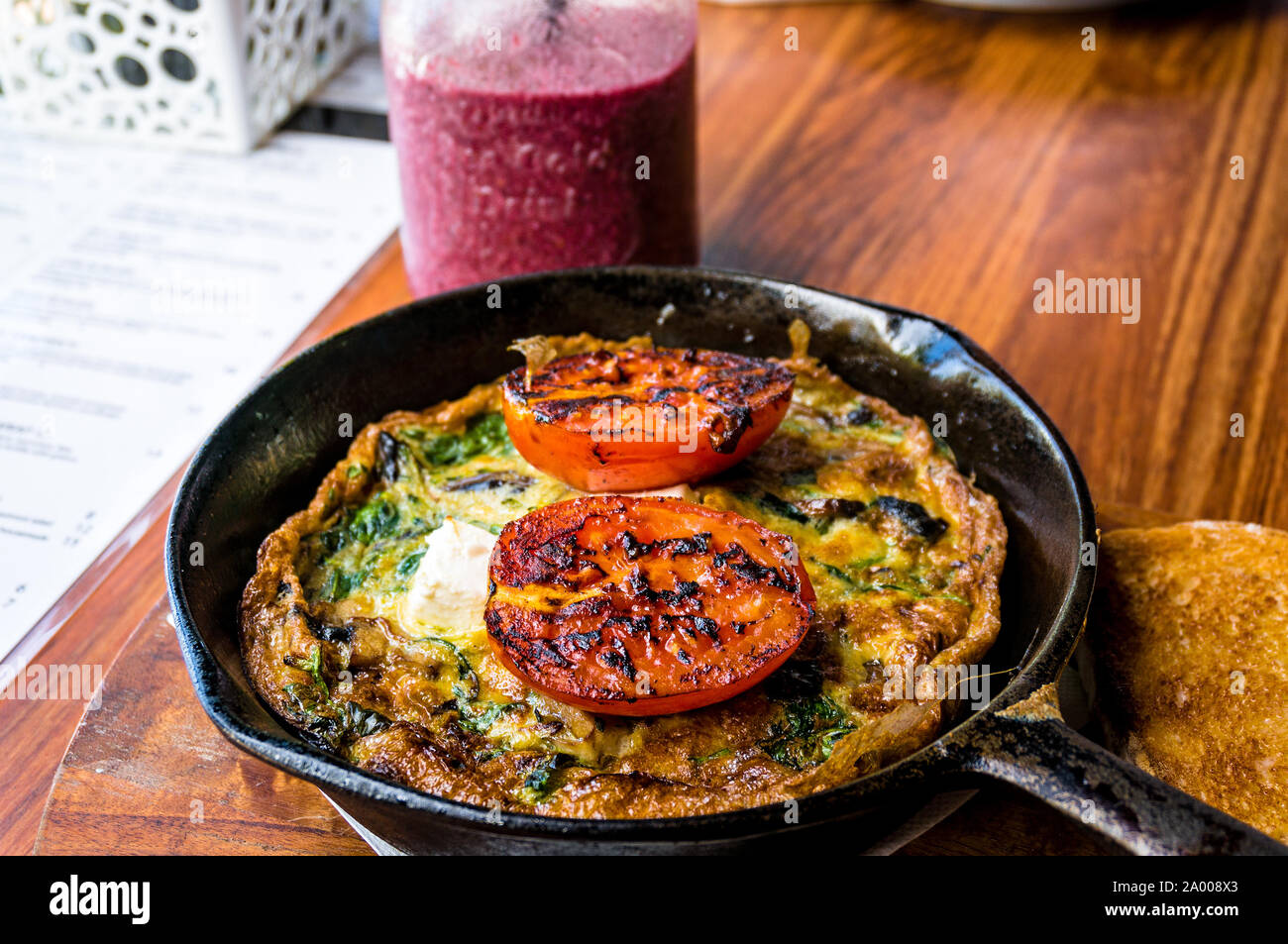 Frittata con pomodoro e verdure su ghisa padella. La colazione rustica frittata con grigliate di pomodoro e le erbe aromatiche e berry smoothie. Il fuoco selettivo Foto Stock