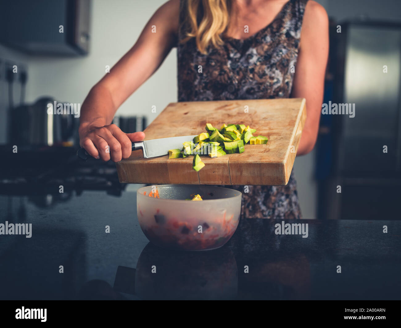 Una giovane donna è aggiunta di un trito di avocado al suo insalata in cucina Foto Stock
