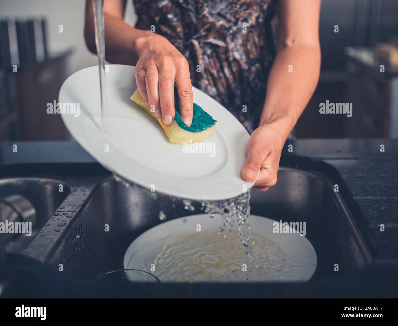 Una giovane donna è la pulizia dei piatti dal lavandino nella sua cucina moderna Foto Stock
