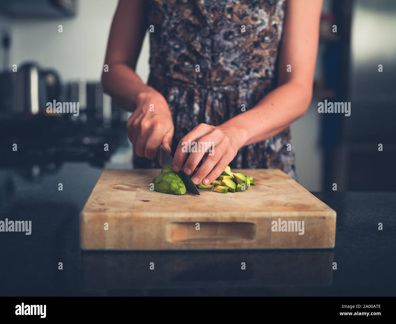 Una giovane donna è la trinciatura avocado nella sua cucina moderna Foto Stock