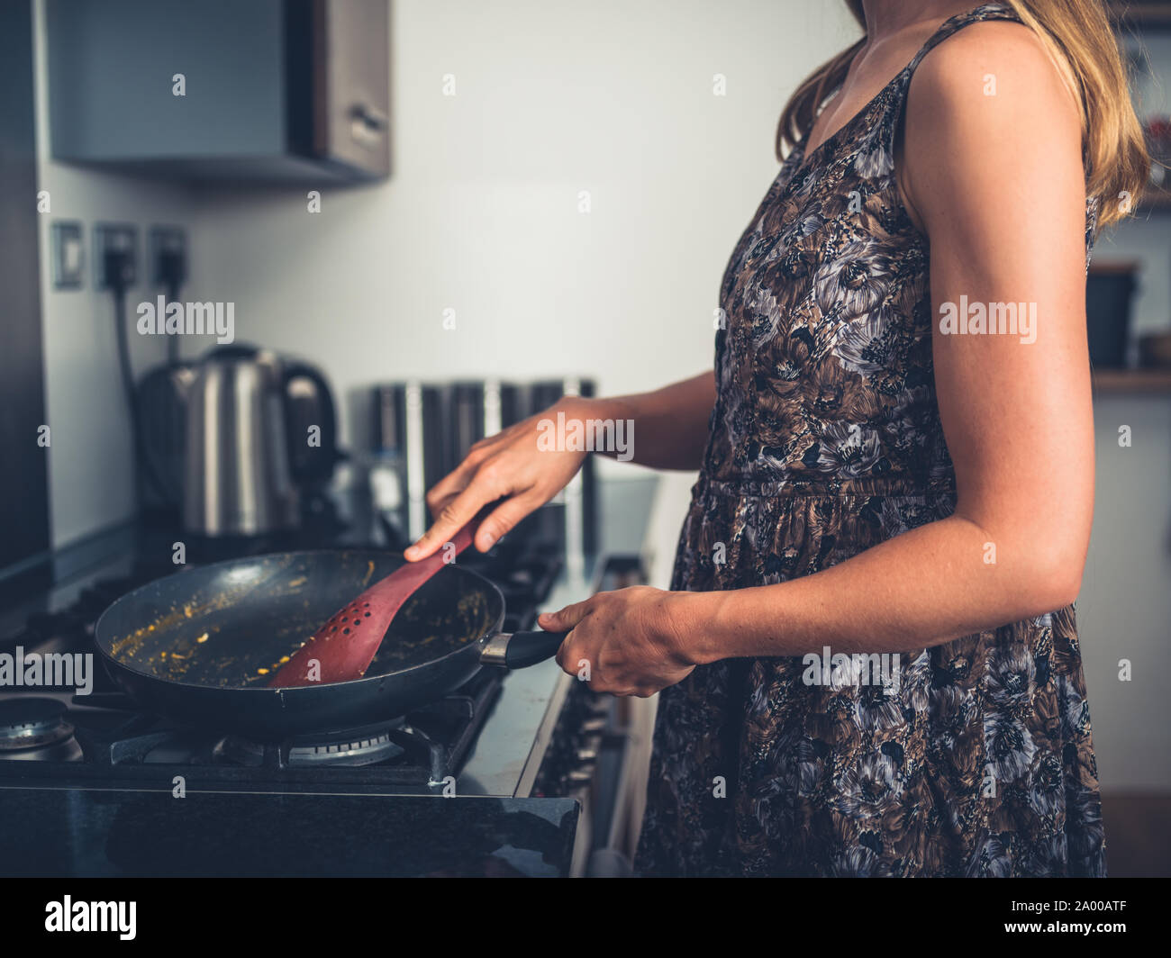 Una giovane donna è la cottura nella sua cucina moderna al fornello a gas con una padella Foto Stock