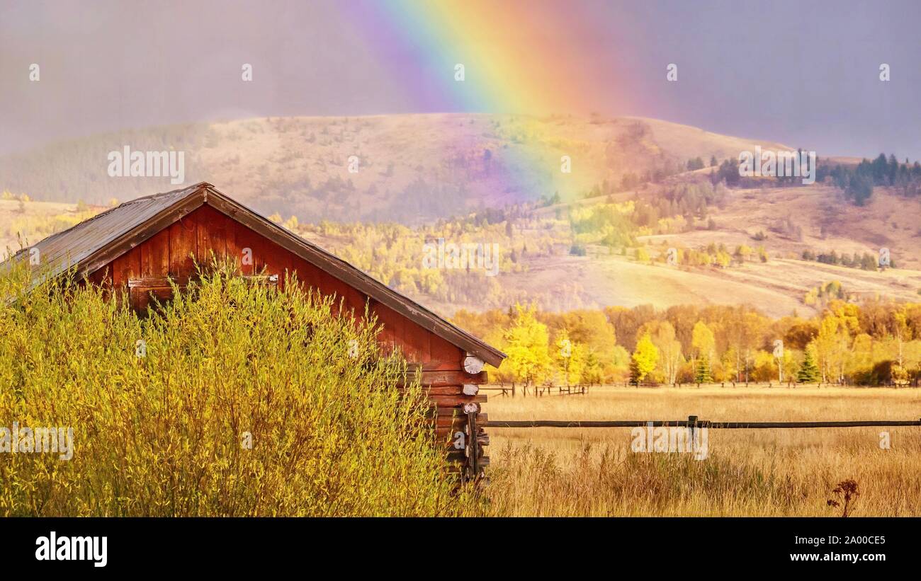 Un bellissimo paesaggio autunnale scena nelle zone rurali del Wyoming, come un arcobaleno riempie il cielo dietro una vecchia cabina in legno. Foto Stock