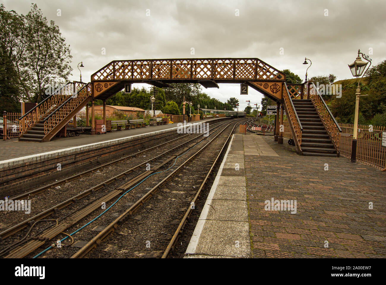 Ponte che attraversa la linea ferroviaria tra due piattaforme ferroviarie con lanterne a piattaforma Foto Stock