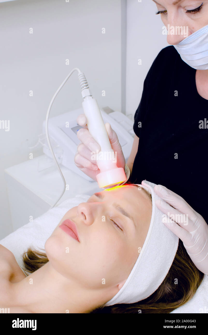 Estetista facendo luce LED rossa la terapia al cliente femmina in un salone  di bellezza, foto del viso per la terapia dei pori della pelle detergente.  Anti-trattamenti di invecchiamento Foto stock -