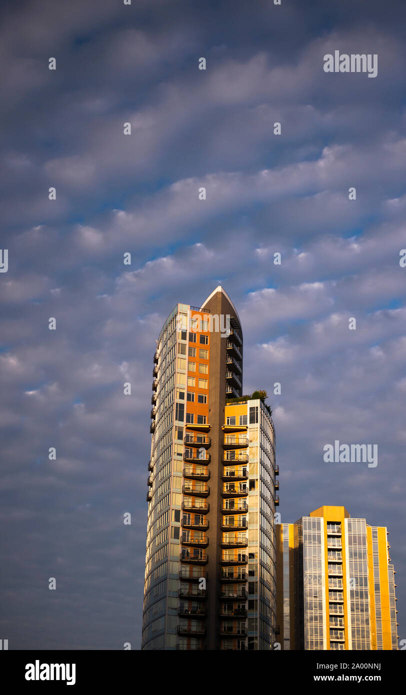 Edifici ad alta geometriche strutturali esterno in vetro e metallo e balconi di riflessione il Sun negli ultimi raggi del sole contro un cielo nuvoloso Foto Stock