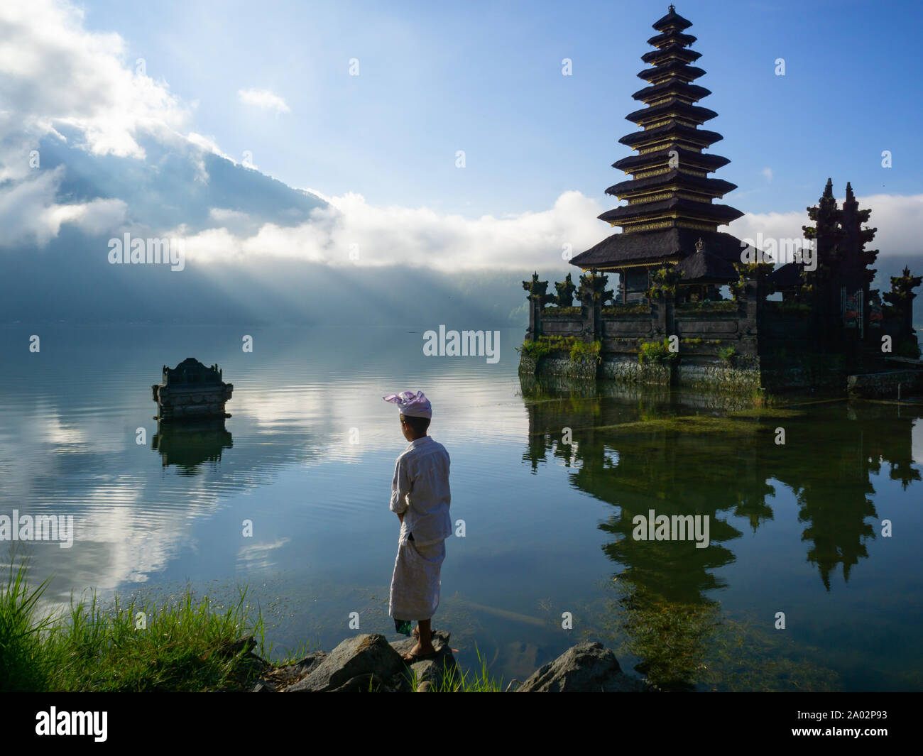 Serena mattina scena vicino al lago con tempio Balinese e non riconosciute giovane uomo con costume Balinese al Lago Batur in Kintamani Bali Indonesia. Foto Stock