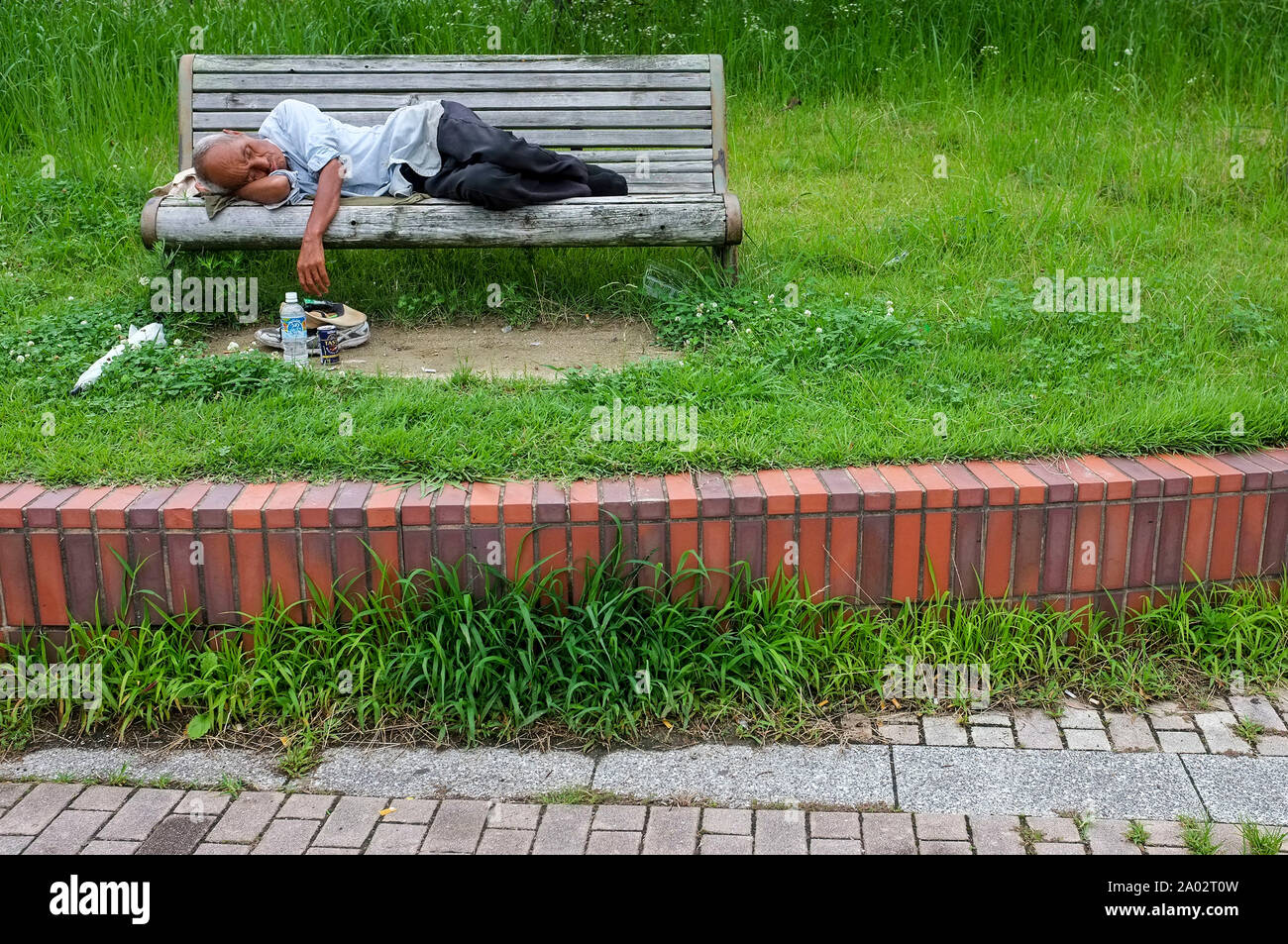 Uomo di dormire su una panchina nel parco, a Fukuoka, Giappone. Foto Stock