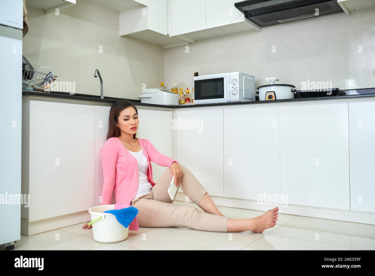 Stanco donna asiatica pulisce il pavimento in cucina Foto Stock