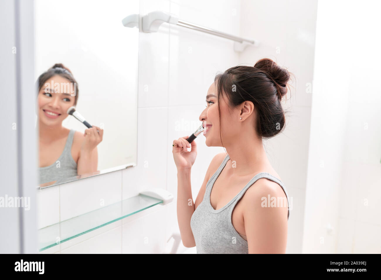Una giovane donna è in piedi di fronte a specchio del bagno e mettendo il trucco. Foto Stock