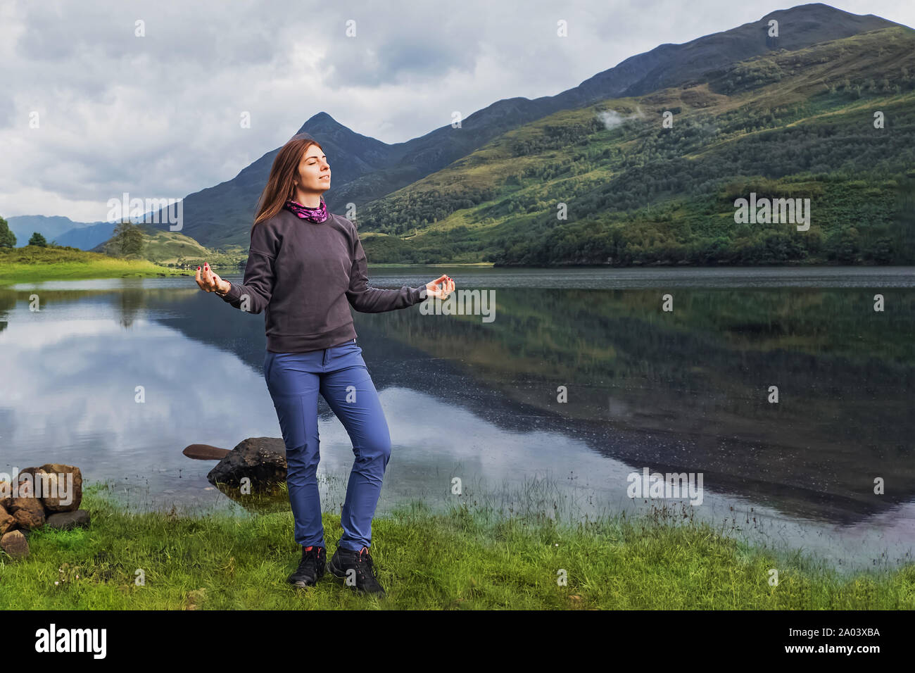 Giovane donna in piedi turistico vicino al wery calma e tranquillità del lago con le sue mani in posizione meditativa e gli occhi chiusi godendo la natura Foto Stock