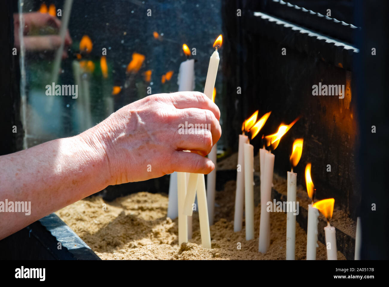 Donna mette mano la candela fiammeggiante con la riflessione sul vetro nella chiesa. La religione. Foto Stock