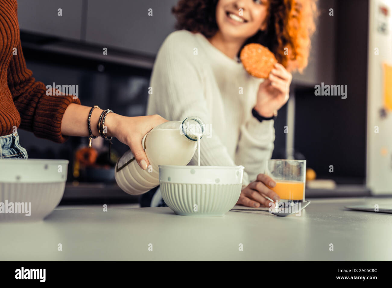 La mano di una giovane donna versando il latte in una ciotola di fronte il suo amico sorridente Foto Stock