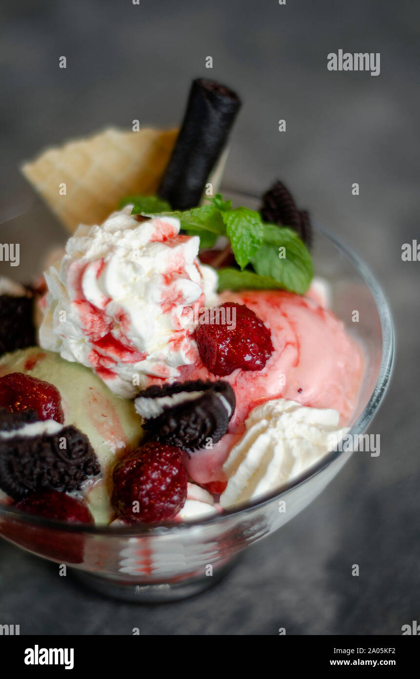 Lampone e pistacchio gelato dessert gelato nel contenitore in vetro con biscotti al cioccolato e frutti di bosco Foto Stock
