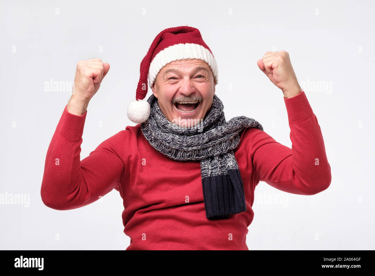 Gioiosa maturo uomo ispanico nel cappello di Natale è felice con doni e gridando wow. In alto le mani entusiasti pongono. Studio shot Foto Stock
