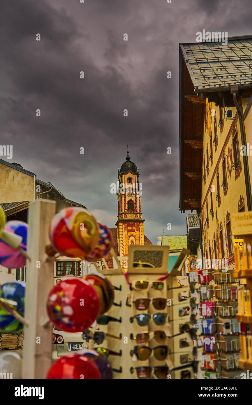 Chiesa bavarese torre davanti un intenzionalmente sfocate stand di souvenir sotto un cielo drammatico Foto Stock