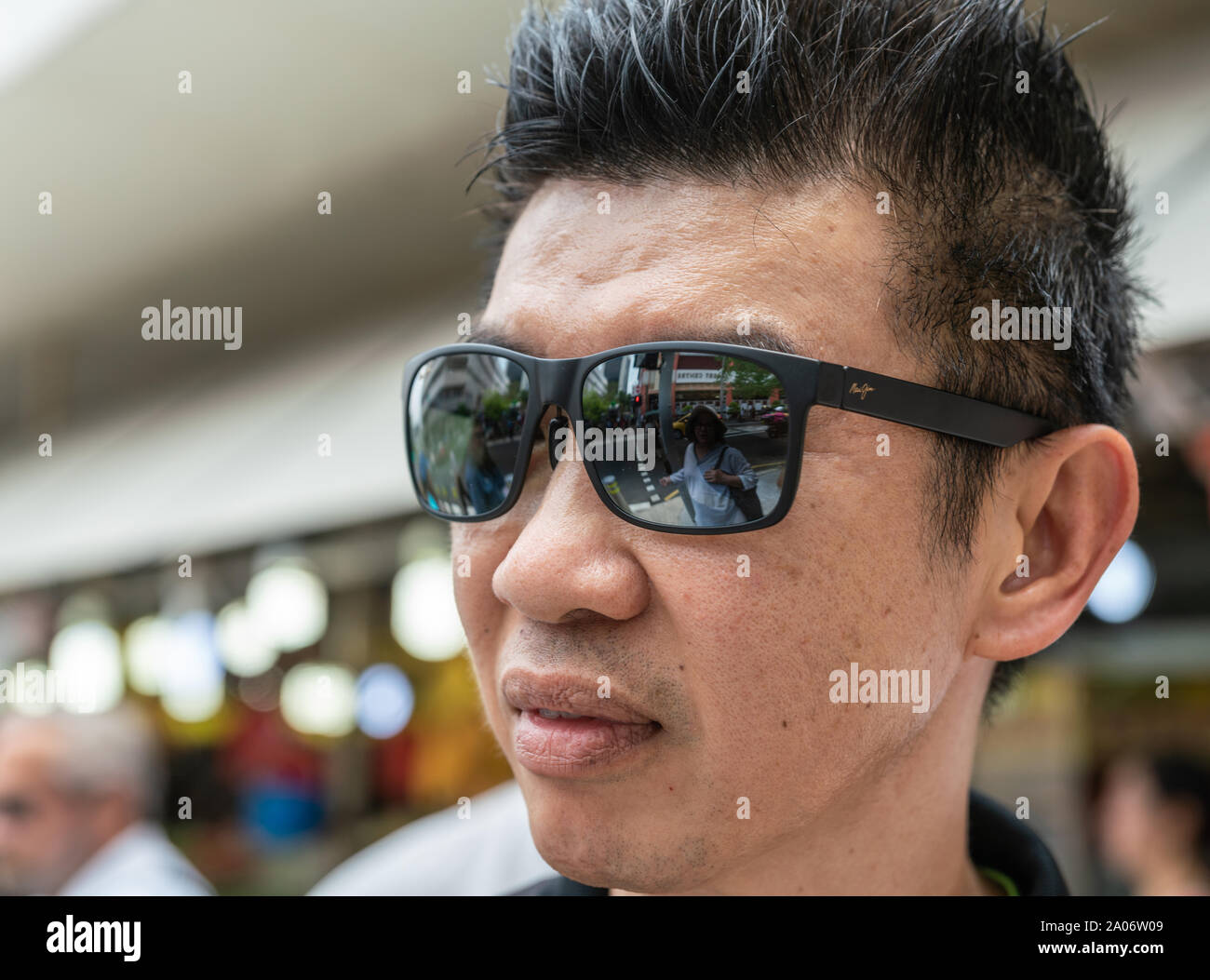 Singapore - Marzo 21, 2019: primo piano del volto del giovane. Black Maui Jim Occhiali da sole riflettono la donna e scene di strada. Foto Stock