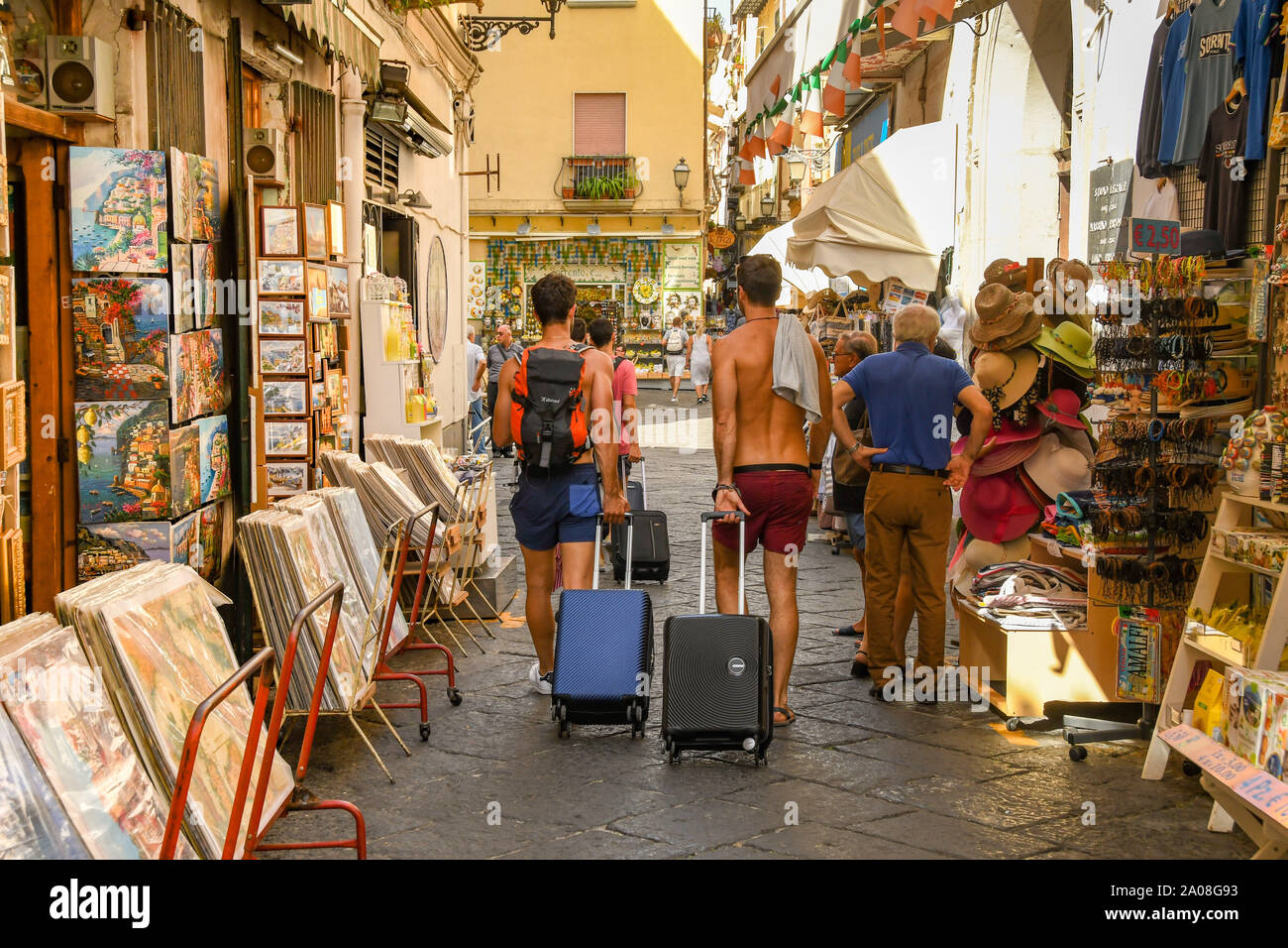 SORRENTO, ITALIA - Agosto 2019: giovani tirando le valigie passato negozi di souvenir del centro storico di Sorrento. Foto Stock