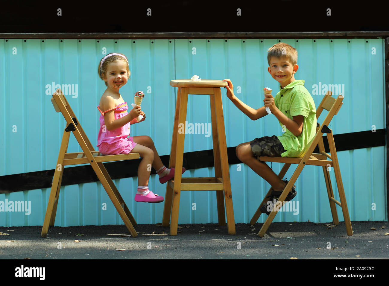 Felice un ragazzo e una ragazza, fratello e sorella, mangiare il gelato in aria aperta marciapiede esterno estate in città cafe Foto Stock
