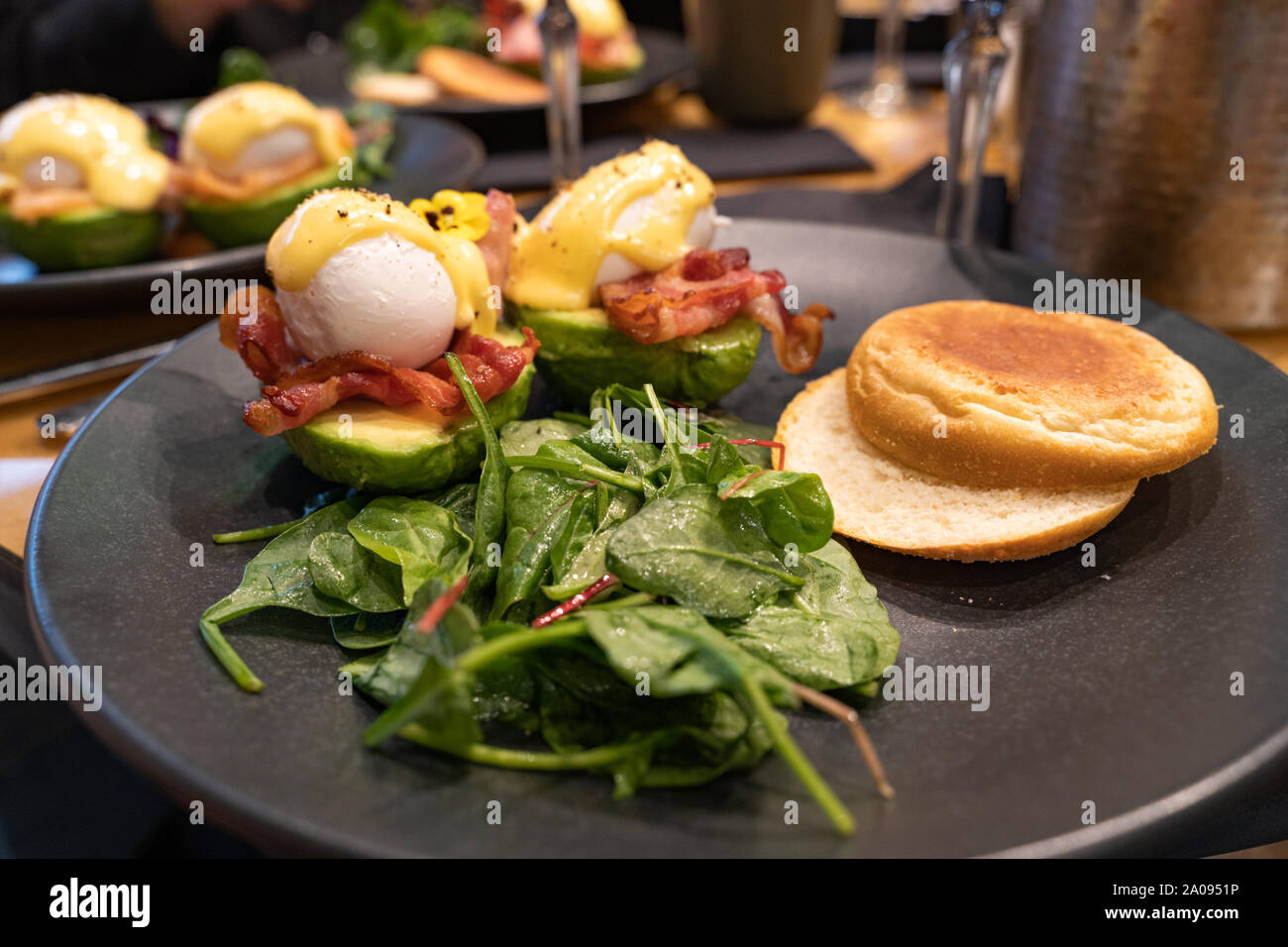 Avocado benedetto. Uovo affogato servita su una metà di avocado con salsa olandese e bacon, pane bun e insalata verde su un lato Foto Stock