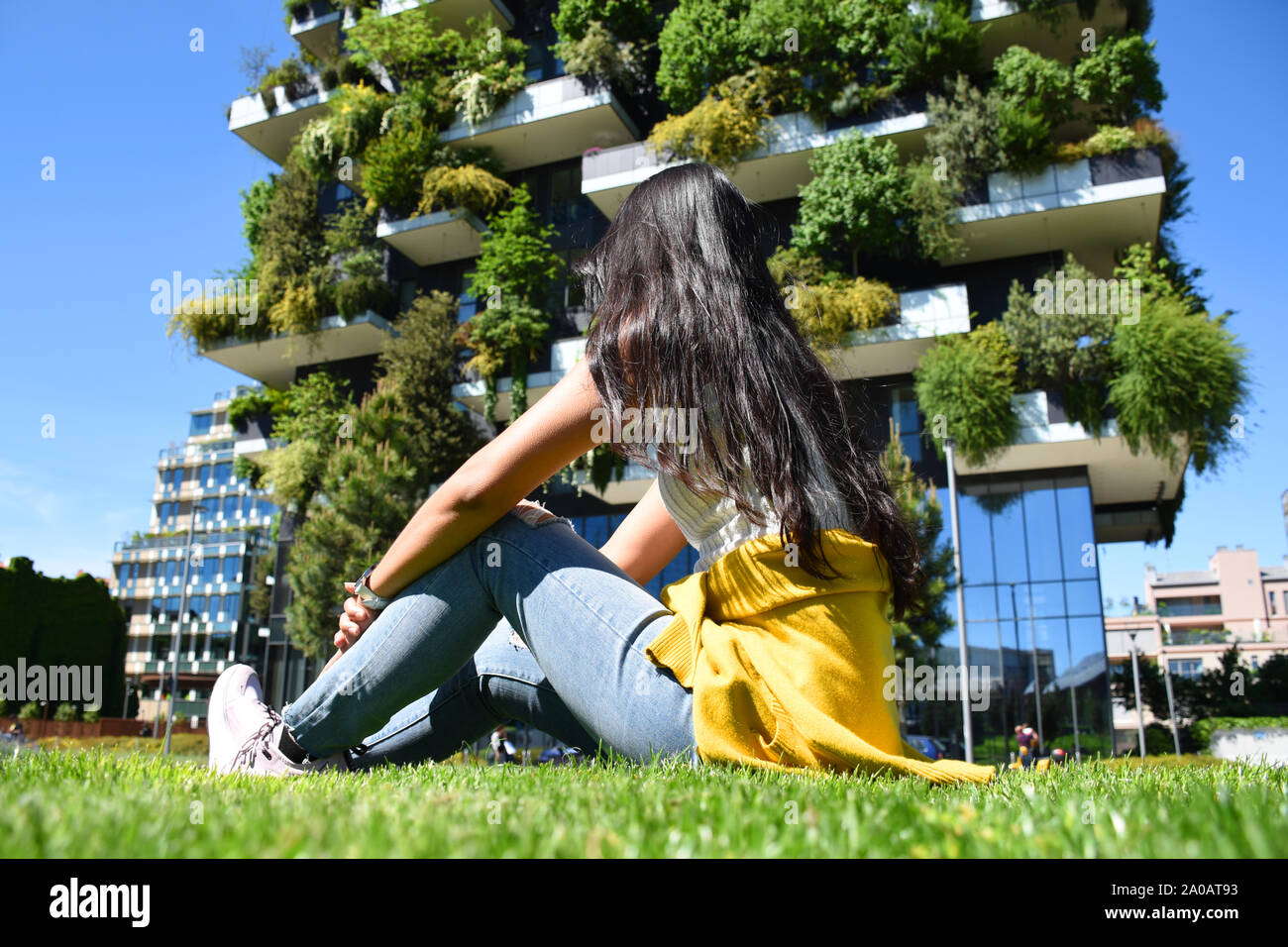 Bella thai conciate bruna è seduto di fronte al Bosco Verticale (Bosco Verticale) torri residenziali e cercando di piantati alberi 900 Foto Stock