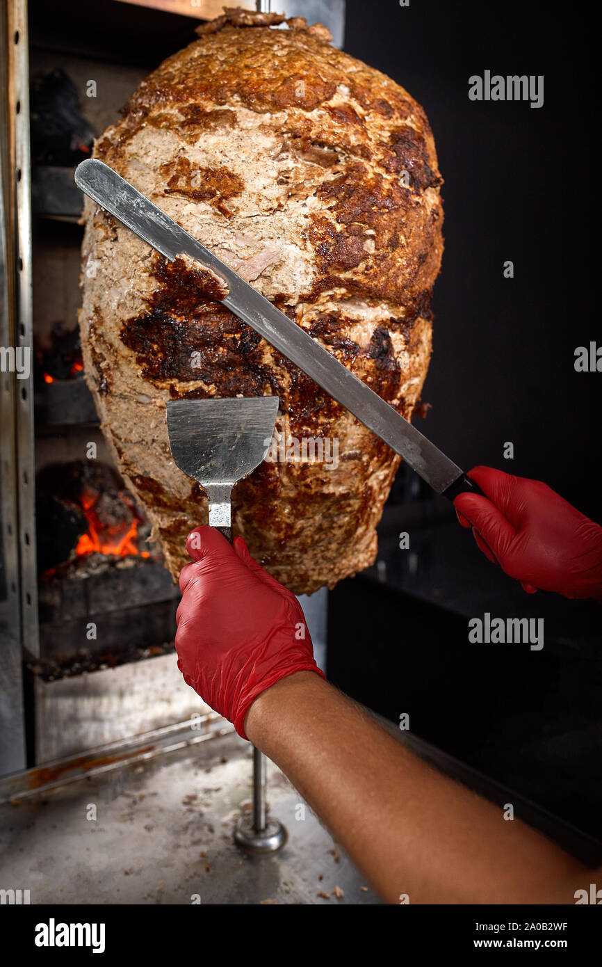 Fritti di carne su uno spiedino per la cottura di donatori o shawarma. Le mani di close-up di tagli di carni in strato sottile Foto Stock