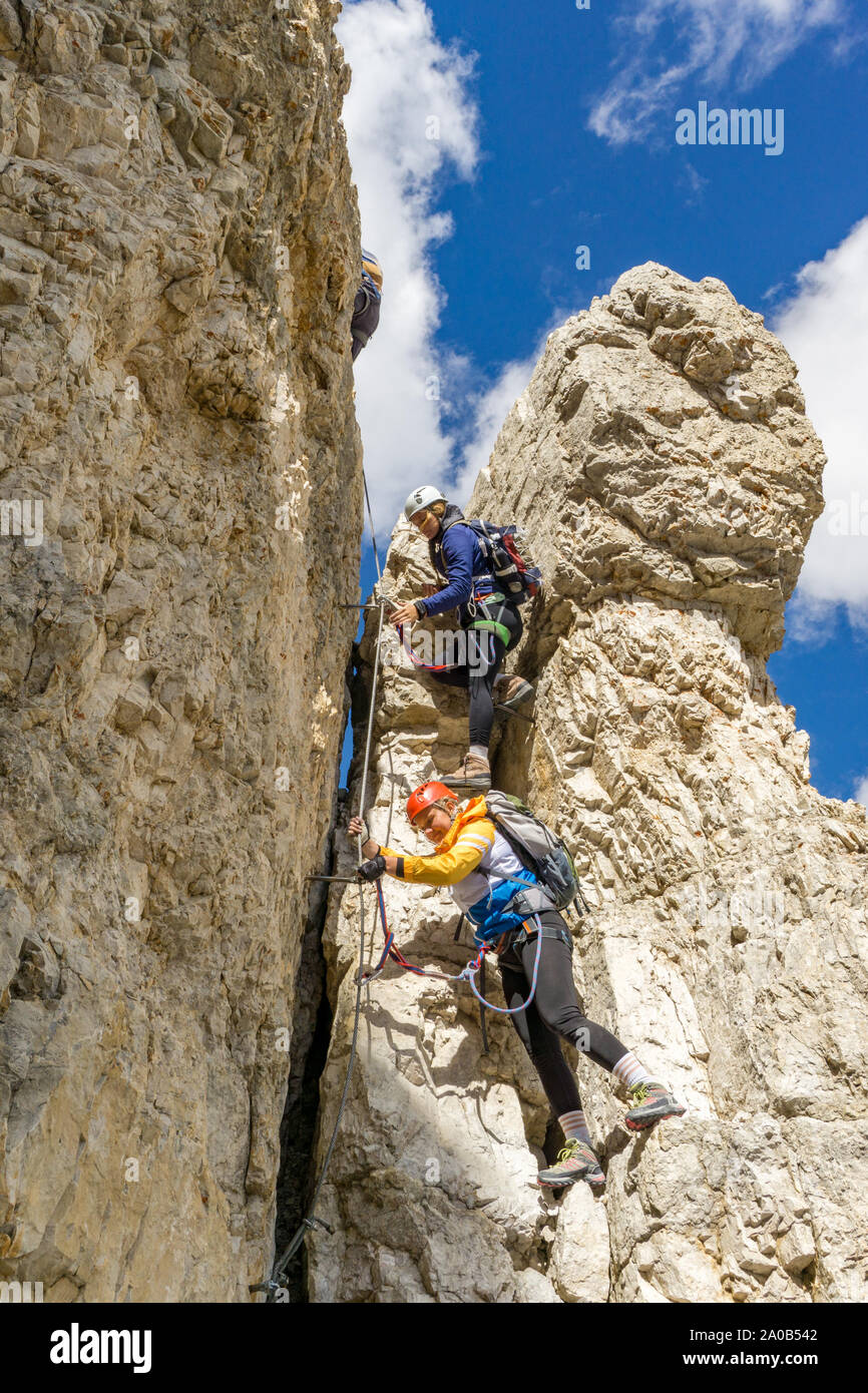 Vista verticale di un attraente arrampicatori femmina su una ripida Via Ferrata delle Dolomiti italiane con una grande vista dietro Foto Stock