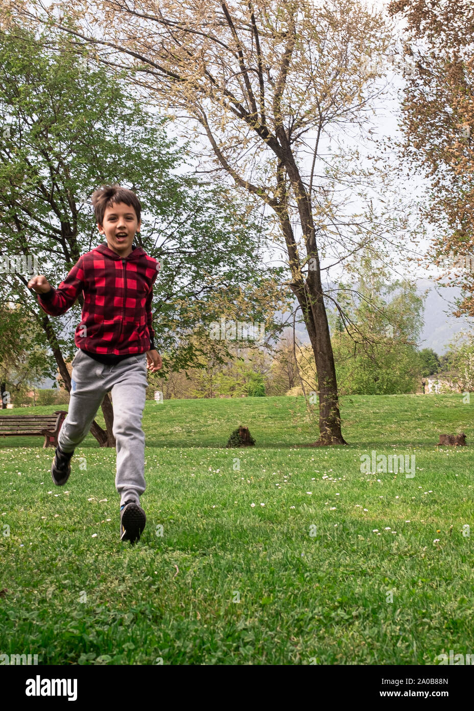 Sorridente giovane ragazzo che corre attraverso il campo erboso, divertendosi, concetti di innocenza e allegria, positivo le emozioni umane. Foto Stock