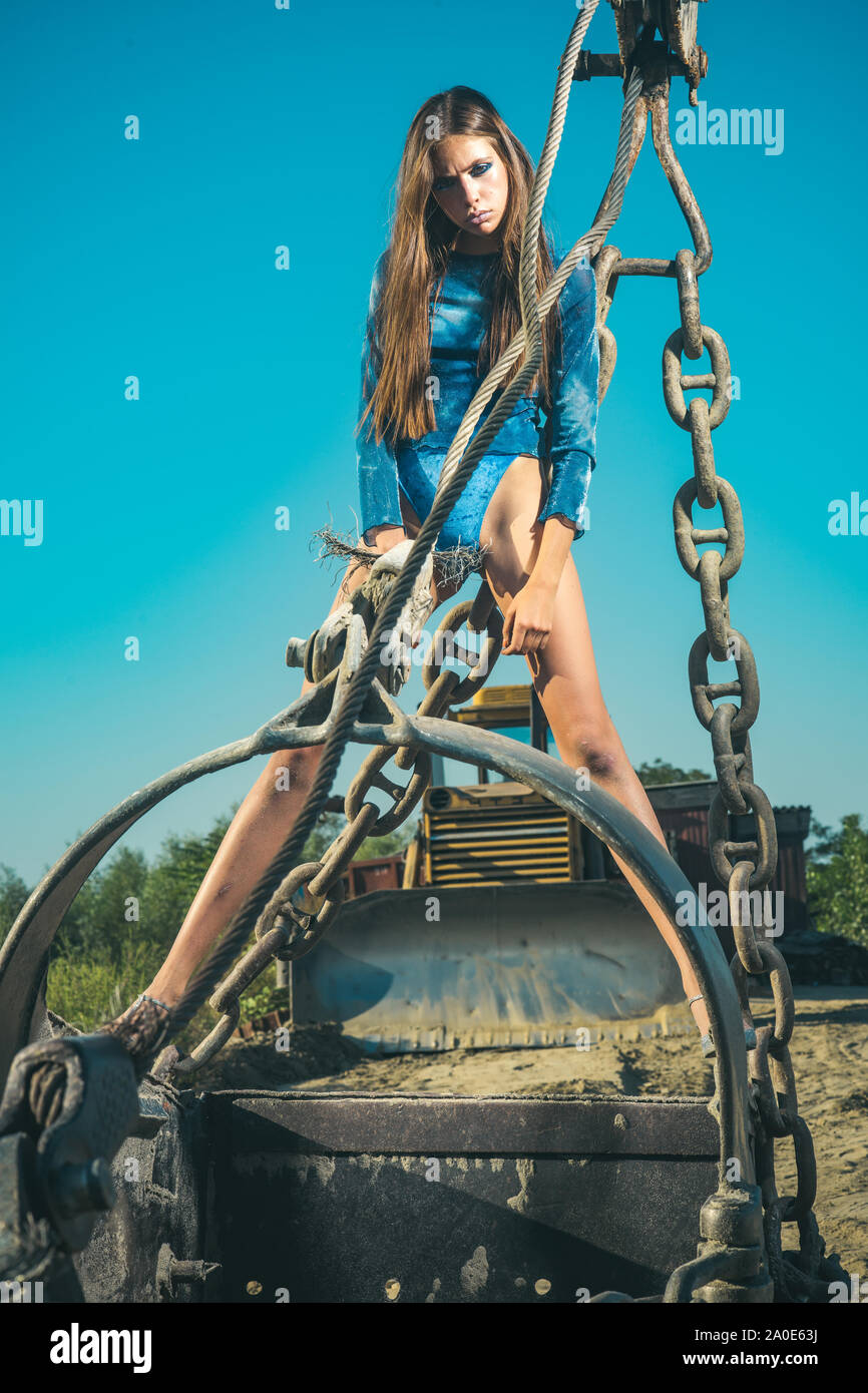 Donna in grande escavatore benna del cielo blu, industria. Donna con capelli lunghi in coppe nella pala, moda. Industria, attrezzature, macchina. Moda e bellezza Foto Stock