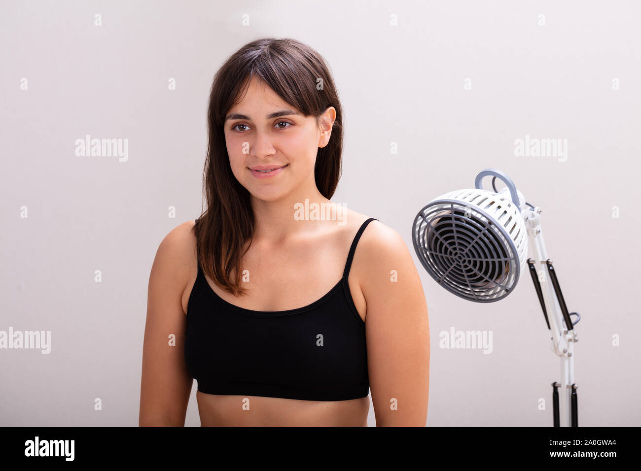 Sorridente giovane donna riceve la radiazione infrarossa di calore lampada luce terapia contro lo sfondo grigio Foto Stock