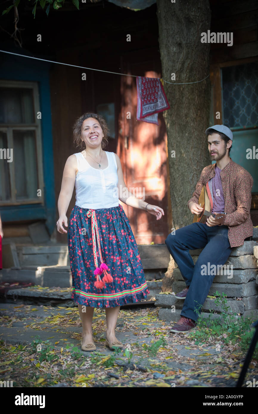 Donna sorridente dancing vicino la casa di paese e un uomo giocando balalaika Foto Stock