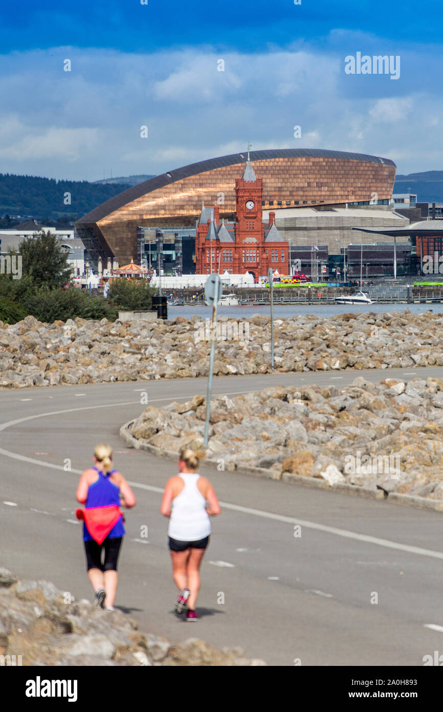 Due guide femmina jog lungo la Baia di Cardiff barrage verso il centro del millennio e Pierhead Buildingl, Glamorgan, Wales, Regno Unito Foto Stock