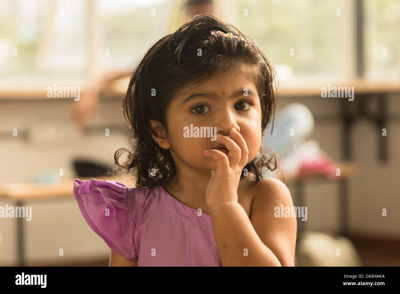 Un simpatico bambina dando uno sguardo innocente verso la telecamera durante una famiglia photo shoot Foto Stock