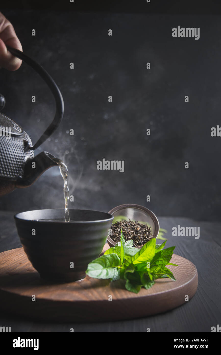 Versare il tè caldo con vapore nella tazza sulla tavola nera. Il tè cinese. Asian ancora in vita. Foto Stock