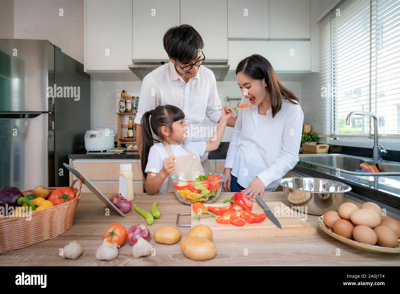 Asian figlie insalata di alimentazione a sua madre e suo padre in stand by quando una famiglia la cottura nella cucina di casa. La vita della famiglia relazione dâ amore, o h Foto Stock