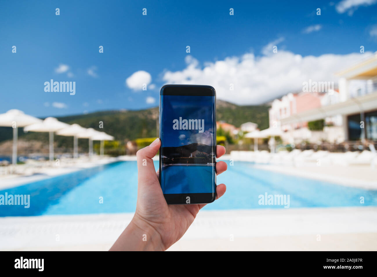 Giovane donna rende la foto della piscina, il cielo blu e il bellissimo paesaggio di sfondo sulla fotocamera dello smartphone, per condividere su internet social media Foto Stock