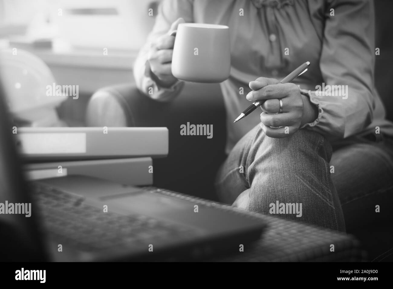 Imprenditrice in abbigliamento casual holding tazza da caffè e penna durante la pianificazione per l'ordinazione online con laptop via internet. Aziendali e finanziarie. Foto Stock